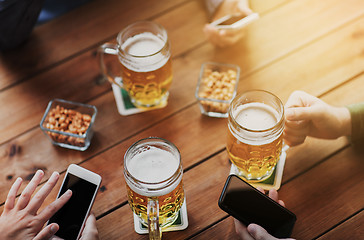 Image showing close up of hands with smartphones and beer at bar