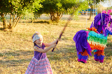 Image showing Young girl at an outdoor party hitting a pinata