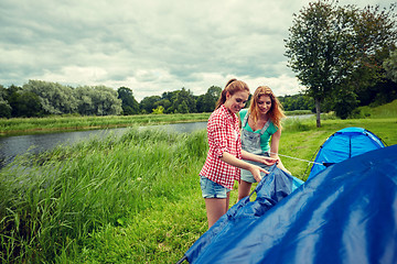 Image showing smiling friends setting up tent outdoors