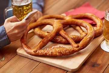 Image showing close up of man with smartphone, beer and pretzels