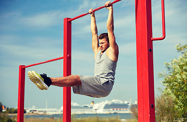 Image showing young man exercising on horizontal bar outdoors