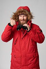 Image showing Man in winter jacket holding binoculars and gesturing thumb up