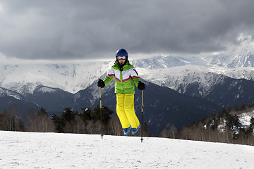 Image showing Young skier jump with ski poles in sun mountains and cloudy gray