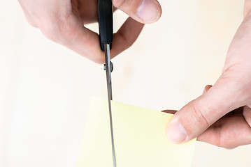 Image showing A man is cutting a sheet of yellow paper using metallic scissors