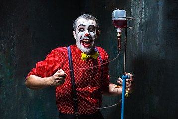 Image showing The scary clown and drip with blood on dack background. Halloween concept