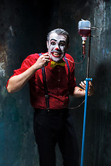 Image showing The scary clown and drip with blood on dack background. Halloween concept