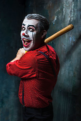 Image showing The scary clown and baseball-bat on dack background. Halloween concept