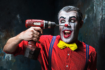 Image showing The scary clown and electric drill on dack background. Halloween concept