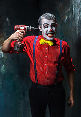 Image showing The scary clown and electric drill on dack background. Halloween concept