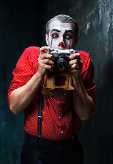 Image showing The scary clown and a camera on dack background. Halloween concept