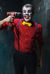 Image showing The scary clown and electric drill on dack background. Halloween concept