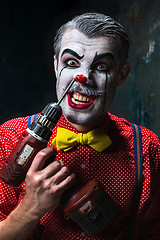 Image showing The scary clown and electric drill on dack background. Halloween concept