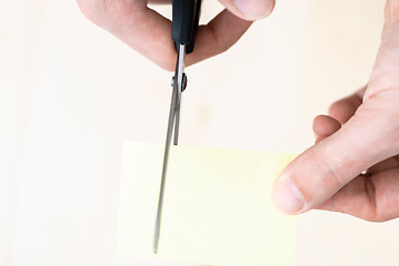 Image showing A man is cutting a sheet of yellow paper using metallic scissors