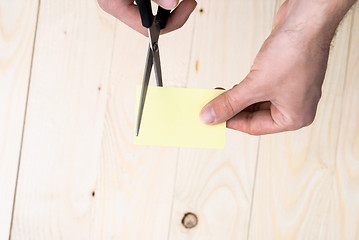 Image showing A man is cutting a sheet of yellow paper using metallic scissors