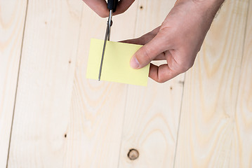 Image showing A man is cutting a sheet of yellow paper using metallic scissors