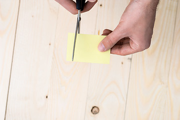 Image showing A man is cutting a sheet of yellow paper using metallic scissors