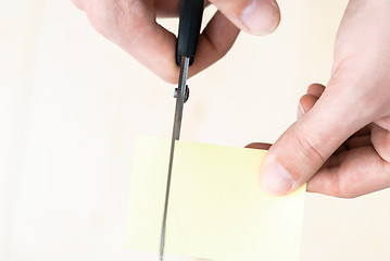 Image showing A man is cutting a sheet of yellow paper using metallic scissors