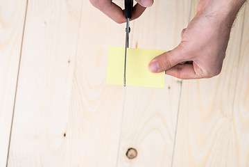 Image showing A man is cutting a sheet of yellow paper using metallic scissors