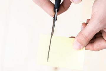 Image showing A man is cutting a sheet of yellow paper using metallic scissors