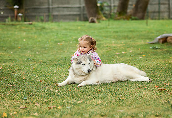 Image showing The little baby girl playing with dog against green grass