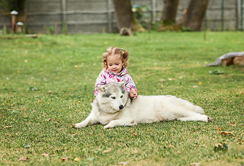 Image showing The little baby girl playing with dog against green grass