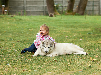 Image showing The little baby girl playing with dog against green grass