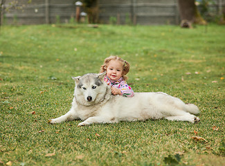 Image showing The little baby girl playing with dog against green grass