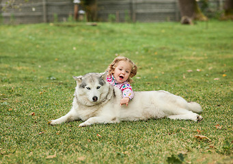 Image showing The little baby girl playing with dog against green grass