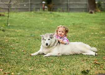 Image showing The little baby girl playing with dog against green grass