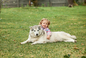 Image showing The little baby girl playing with dog against green grass