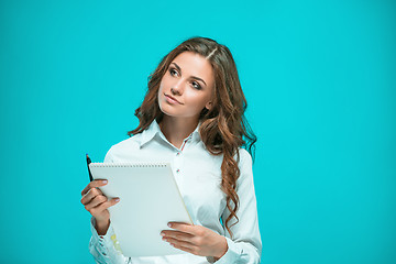 Image showing The smiling young business woman with pen and tablet for notes on blue background