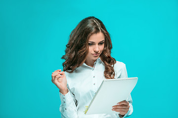 Image showing The smiling young business woman with pen and tablet for notes on blue background