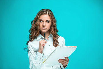 Image showing The thoughtful young business woman with pen and tablet for notes on blue background