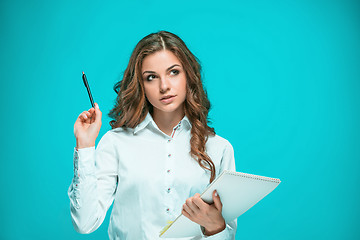 Image showing The thoughtful young business woman with pen and tablet for notes on blue background