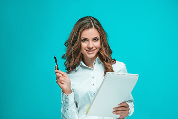 Image showing The smiling young business woman with pen and tablet for notes on blue background