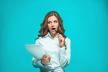 Image showing The thoughtful young business woman with pen and tablet for notes on blue background