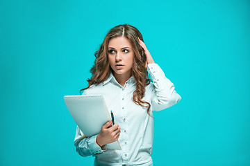 Image showing The thoughtful young business woman with pen and tablet for notes on blue background