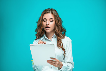 Image showing The thoughtful young business woman with pen and tablet for notes on blue background