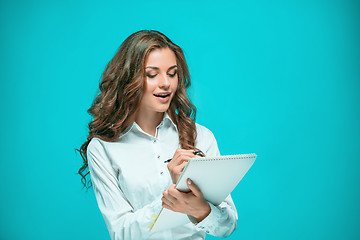 Image showing The smiling young business woman with pen and tablet for notes on blue background