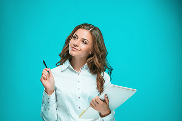 Image showing The smiling young business woman with pen and tablet for notes on blue background