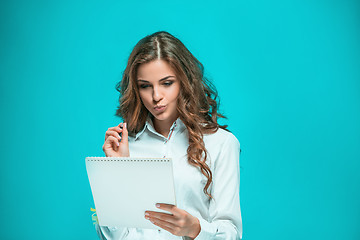 Image showing The thoughtful young business woman with pen and tablet for notes on blue background