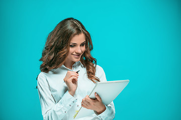 Image showing The smiling young business woman with pen and tablet for notes on blue background