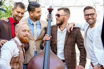 Image showing Group of five stylish male friends talking and having fun outdoors, holding double bass