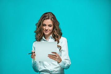 Image showing The smiling young business woman with pen and tablet for notes on blue background