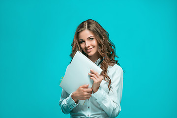 Image showing The smiling young business woman with pen and tablet for notes on blue background