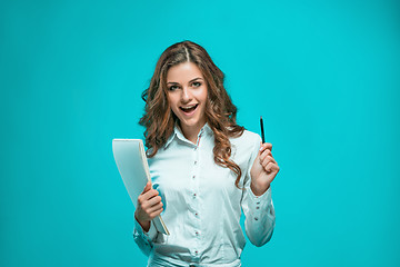 Image showing The smiling young business woman with pen and tablet for notes on blue background