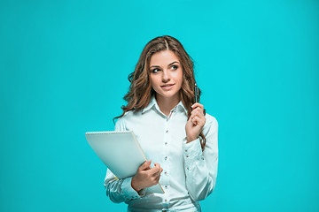 Image showing The smiling young business woman with pen and tablet for notes on blue background