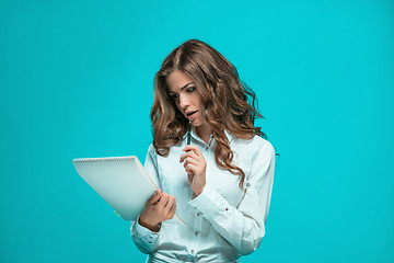 Image showing The thoughtful young business woman with pen and tablet for notes on blue background