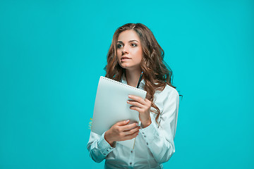 Image showing The thoughtful young business woman with pen and tablet for notes on blue background