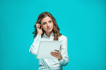 Image showing The thoughtful young business woman with pen and tablet for notes on blue background